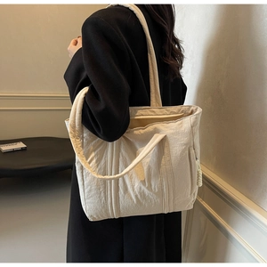 Detail view of large cream tote bag with nylon texture and woven decorative pendant