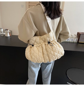 Detail view of cream quilted puffer bag featuring a drawstring closure and a wide canvas strap