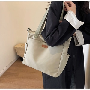 Detail of minimalist beige tote bag with leather logo patch and green woven handles