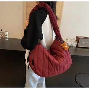 Side view of dark red quilted puffer bag on model with cute plush bear charm