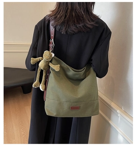 Detailed back view of a green canvas hobo bag with leather strap and plush charm