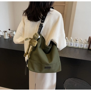 Detail of dark green canvas hobo bag with adjustable leather strap and plush frog charm
