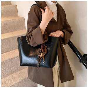 Détail d'un sac à bandoulière en cuir PU brillant noir avec un pendentif tissé élégant
