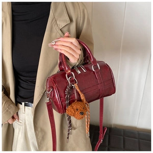 Detail of burgundy PU leather barrel bag with plush dog charm and silver hardware
