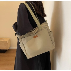 Detail of canvas tote bag with side pocket and brown leather logo patch on shoulder strap