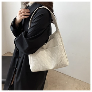Close-up of cream woven PU leather shoulder bag with wide strap on a black coat