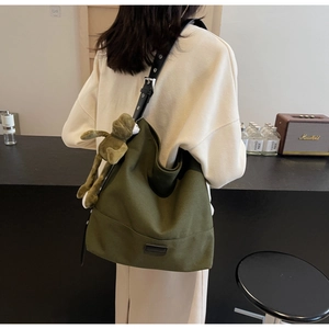 Detail of dark green canvas tote bag with adjustable black strap and green frog plush charm