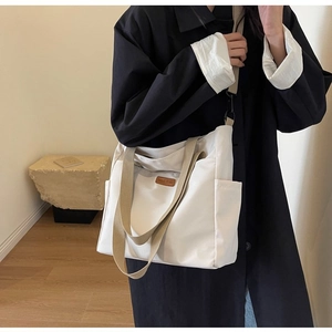 Close-up of white canvas tote bag featuring brown leather patch and adjustable shoulder strap