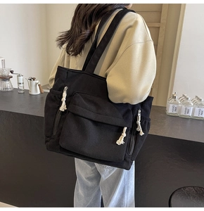 Détail du sac fourre-tout en velours côtelé noir avec poche frontale et tirettes à nœuds blancs