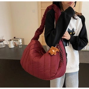 Detail of burgundy quilted puffer crossbody bag with a cute plush bear charm