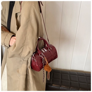 Close-up of burgundy cylindrical handbag featuring a plush bear charm and metallic zipper
