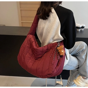 Detail of burgundy quilted shoulder bag with a brown teddy bear charm and striped rope accessory