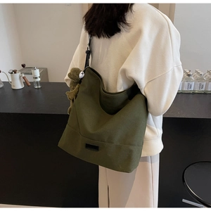 Detail of dark green canvas tote bag with adjustable strap and cute frog plush pendant