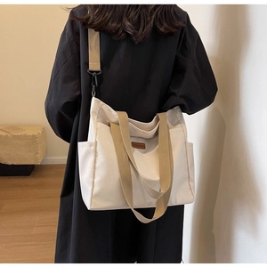 Detail of off-white canvas tote with khaki handles and adjustable strap on a model