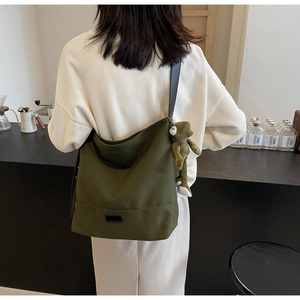 Detail of forest green canvas shoulder bag featuring a cute frog plush charm and black strap