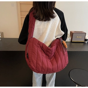 Detail of burgundy quilted crescent bag with vertical stripes and teddy bear charm