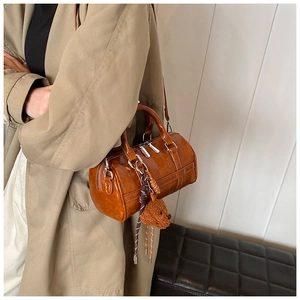 Detail view of a brown PU leather barrel bag with a plush dog charm and woven strap