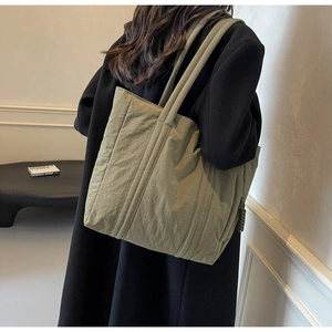 Detailed side view of an olive green quilted nylon tote bag worn by a model in a room