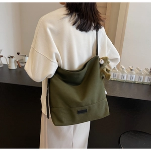 Olive green canvas tote bag with black strap and plush bear accessory in a cozy cafe