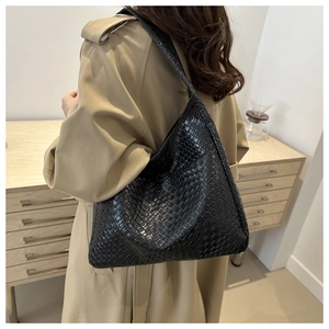 Detail of a large black woven PU leather hobo bag worn by a model in a minimalist home setting