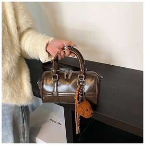 Detail of dark brown wax leather cylinder bag with dual handles and teddy plush charm