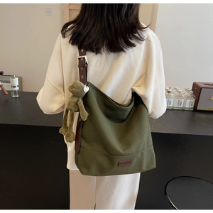 Detail view of military green canvas hobo bag with brown leather strap and frog pendant