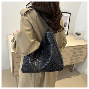 Large black hobo shoulder bag with crocodile texture worn by model in a stylish trench coat