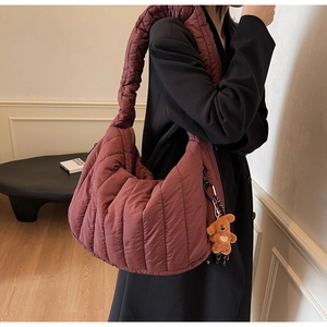 Detail of burgundy quilted puffer hobo bag featuring thick shoulder strap and plush bear charm