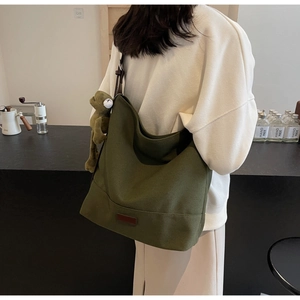 Detail of olive green canvas hobo bag with plush frog pendant and leather logo patch