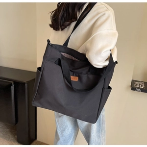 Close-up of black canvas tote bag with brown leather logo patch and side pocket
