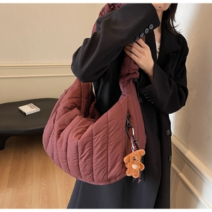 Detail of burgundy quilted shoulder bag with plush bear charm and wide strap on model