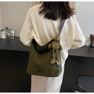 Detail view of large dark green canvas tote bag featuring a plush frog charm and leather straps