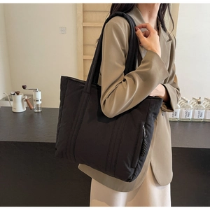 Detail shot of a black quilted shoulder bag with side zipper pocket on a model