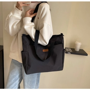 Detail view of a black canvas tote bag with side pockets and elegant brown leather logo patch