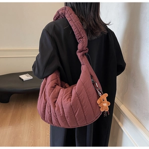 Detail view of burgundy quilted puffer bag with plush bear charm worn by a model