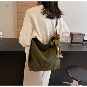 Detail of olive green canvas tote bag with brown leather patch and plush frog pendant