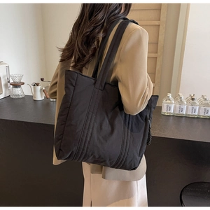 Detail view of large black nylon tote bag on shoulder showing soft textured fabric