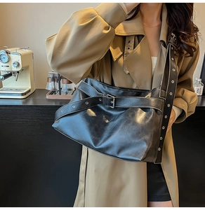Detail of black leather shoulder bag featuring metal eyelet straps and buckle in a retro style
