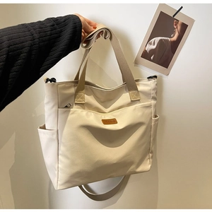Detail of minimalist beige canvas tote bag with brown leather logo and side pocket