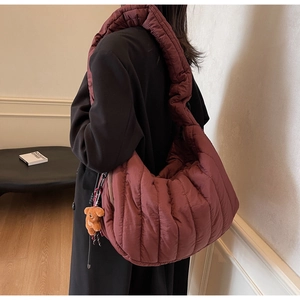 Detail view of burgundy quilted crescent bag with plush bear charm and padded shoulder strap