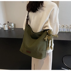 Detail of dark green canvas tote bag featuring a cute plush frog charm and leather base