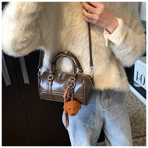 Detail of dark brown glossy PU leather cylinder bag with a cute teddy bear charm