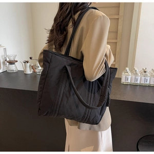 Detail of a black fabric tote bag worn by a model in a minimalist lifestyle setting