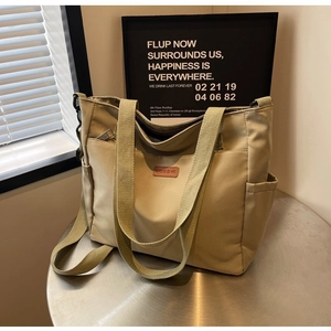 Detail of khaki canvas tote bag featuring side pockets and a leather logo patch