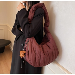 Detail of burgundy quilted puffer bag with brown teddy bear charm on model shoulder
