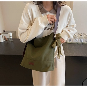 Detail of olive green canvas tote bag with brown leather strap and cute frog pendant