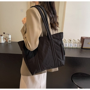 Detailed view of black nylon tote bag featuring vertical stitching and braided cord accents