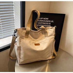 Close-up of cream nylon tote bag with side pockets and premium leather logo tag details