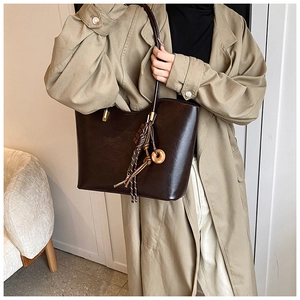Détail d'un sac cabas en cuir PU marron foncé avec breloques porté avec un trench-coat