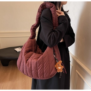 Detailed view of dark red quilted puffer bag with a cute brown plush bear charm